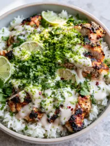 Top-down view of a modern ceramic bowl filled with steaming jasmine rice and charred Coconut Chicken slices with lime zest.