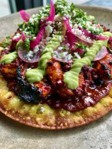 Close-up of seared chipotle shrimp on a crispy tostada with translucent radish slices and cotija cheese. (chipotle shrimp tostadas)