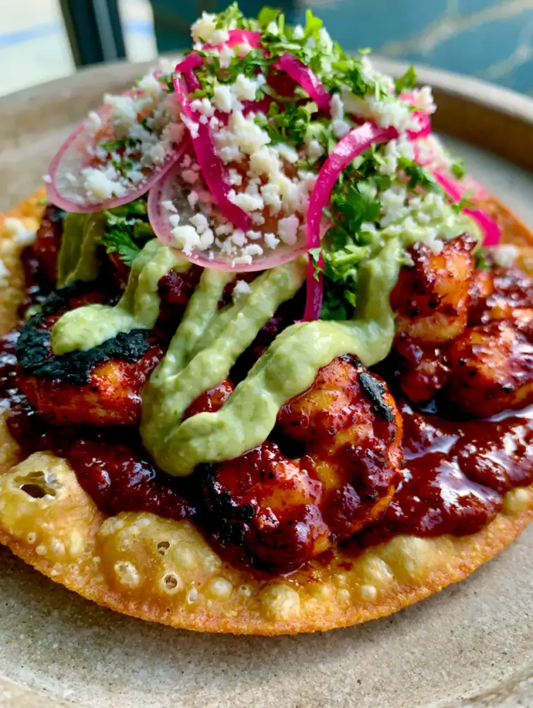 Top view of a single gourmet chipotle shrimp tostada showing the thick golden-brown crispy fried corn tortilla and cilantro garnish.