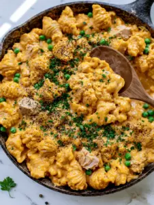 Close up of a wooden spoon lifting ridged pasta shells coated in thick cheddar sauce from a tuna helper dish.