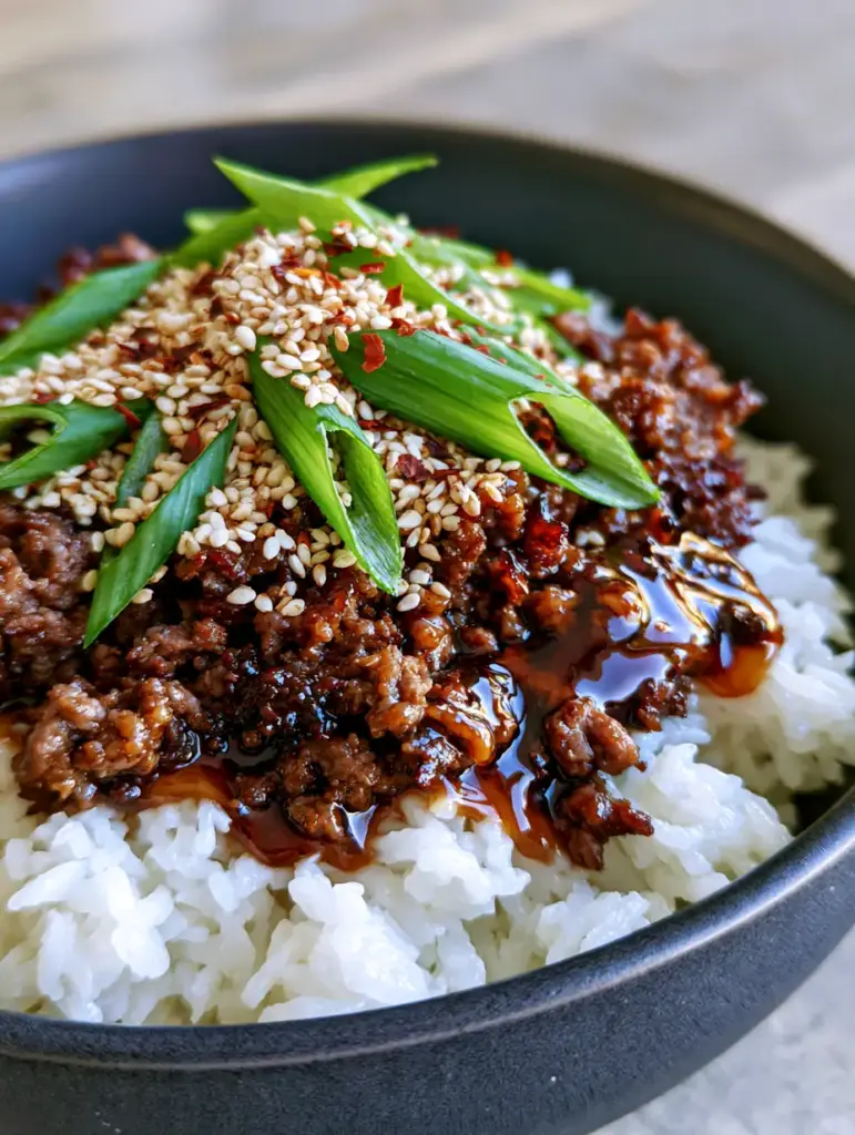 Steaming jasmine rice topped with seared beef crumbles in a charcoal ceramic bowl.