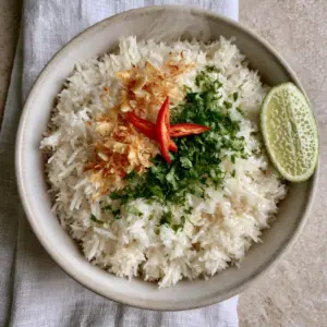 Close-up of glistening long-grain jasmine rice with coconut glaze and red chili slices. (Coconut Rice recipe)