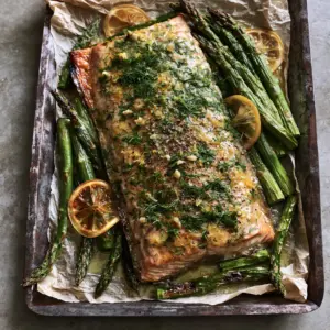 Top-down view of a salmon fillet with glistening garlic butter glaze and vibrant green charred asparagus on crumpled parchment. (Sheet pan lemon garlic butter salmon)