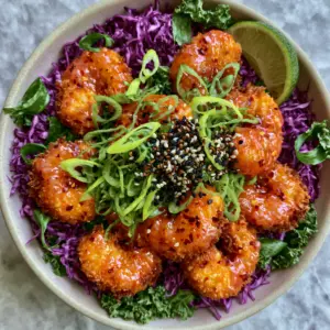 Close up of air-fried panko shrimp in a semi-translucent orange-pink sauce with visible chili flakes. (Bang Bang shrimp recipe)
