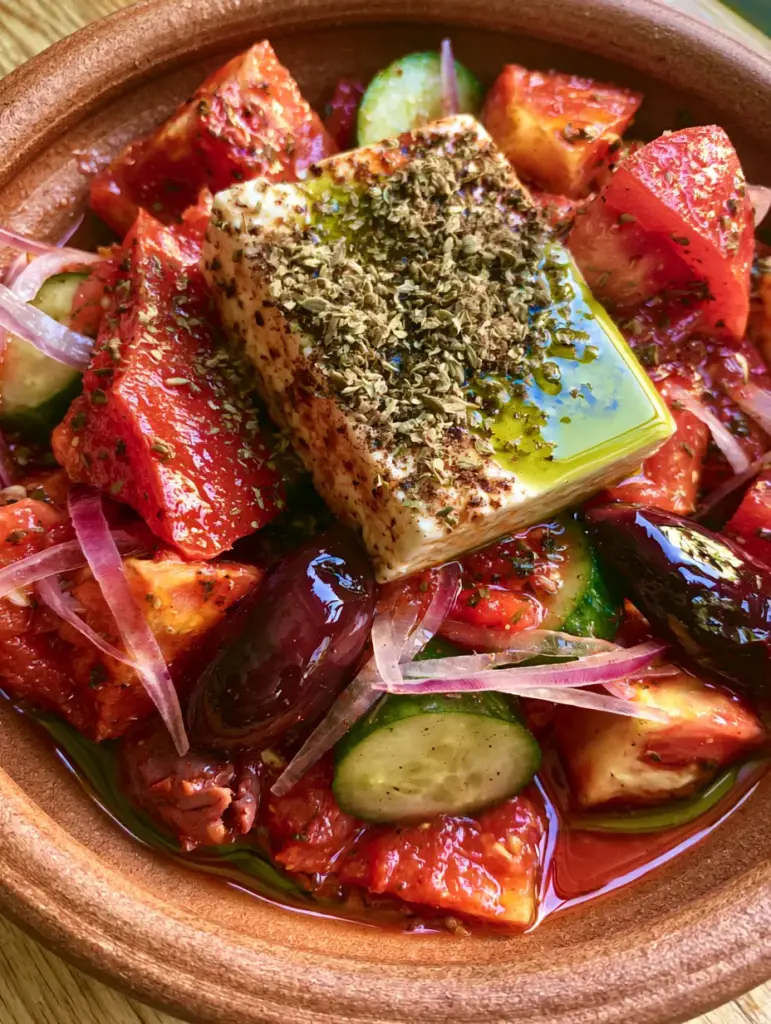 Close-up of a thick slab of feta cheese drizzled with olive oil and dried oregano on a Greek salad.
