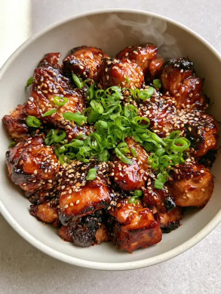 Close-up of charred chicken pieces in a thick teriyaki glaze with sesame seeds and bias-cut scallions.
