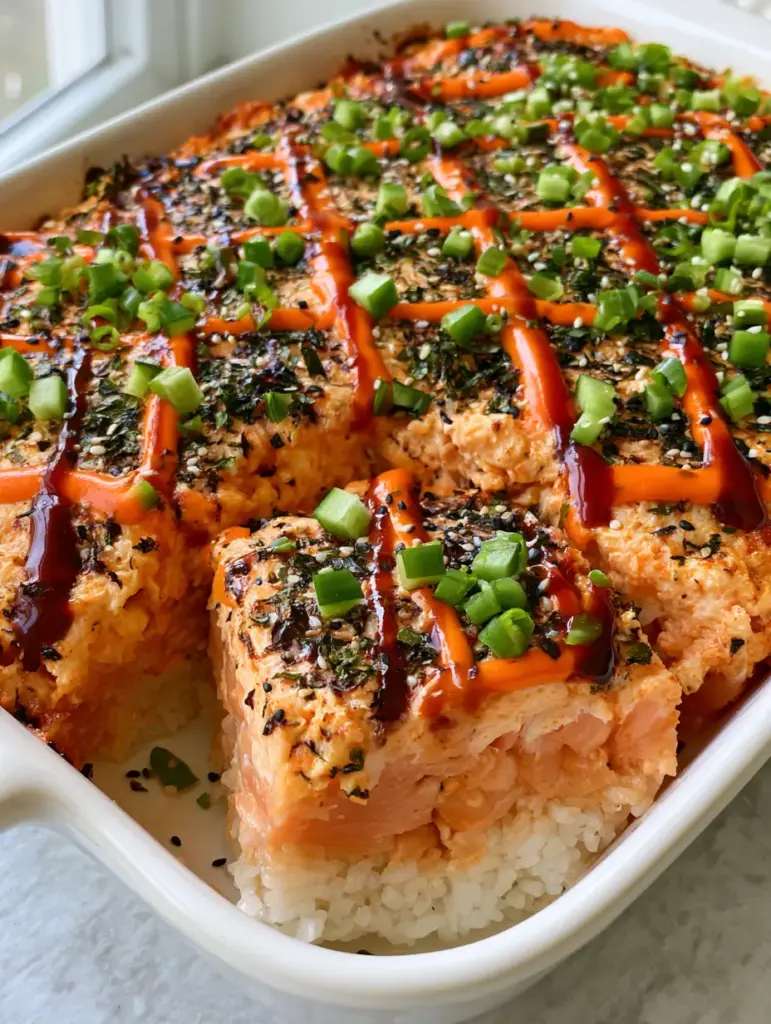 A square serving of sushi bake being lifted out to reveal the pearly white rice and pink salmon cross-section.