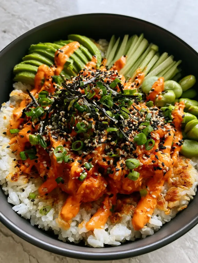 Side view of a spicy tuna rice bowl in a charcoal ceramic bowl showing precise sections of avocado and edamame.