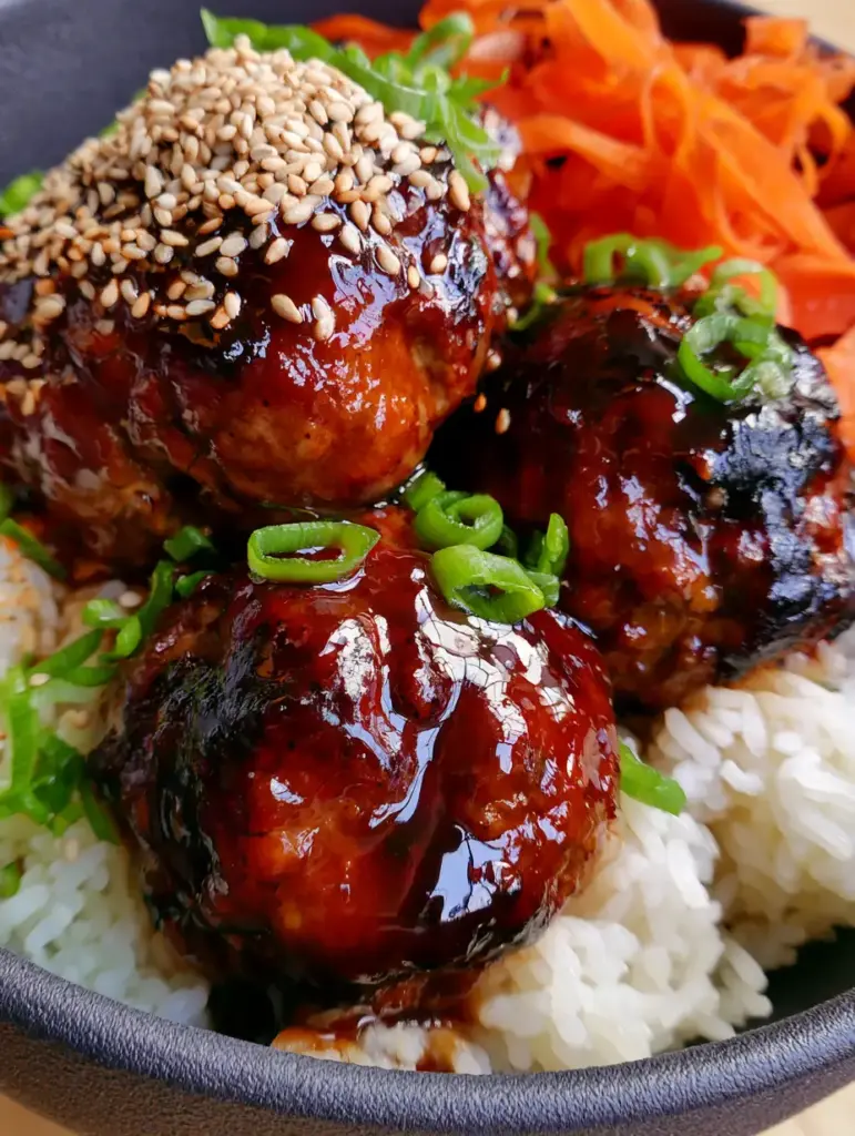 Korean BBQ Meatball Rice Bowls in a charcoal ceramic bowl with vibrant orange carrot ribbons and green scallions.