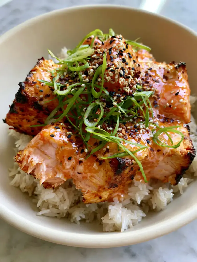 Bang Bang Salmon Recipe: Crispy Air-Fried Bites with Spicy Creamy Sauce 1 Close up view of the vibrant orange-pink bang bang sauce and garnish of sesame seeds and scallions on salmon.