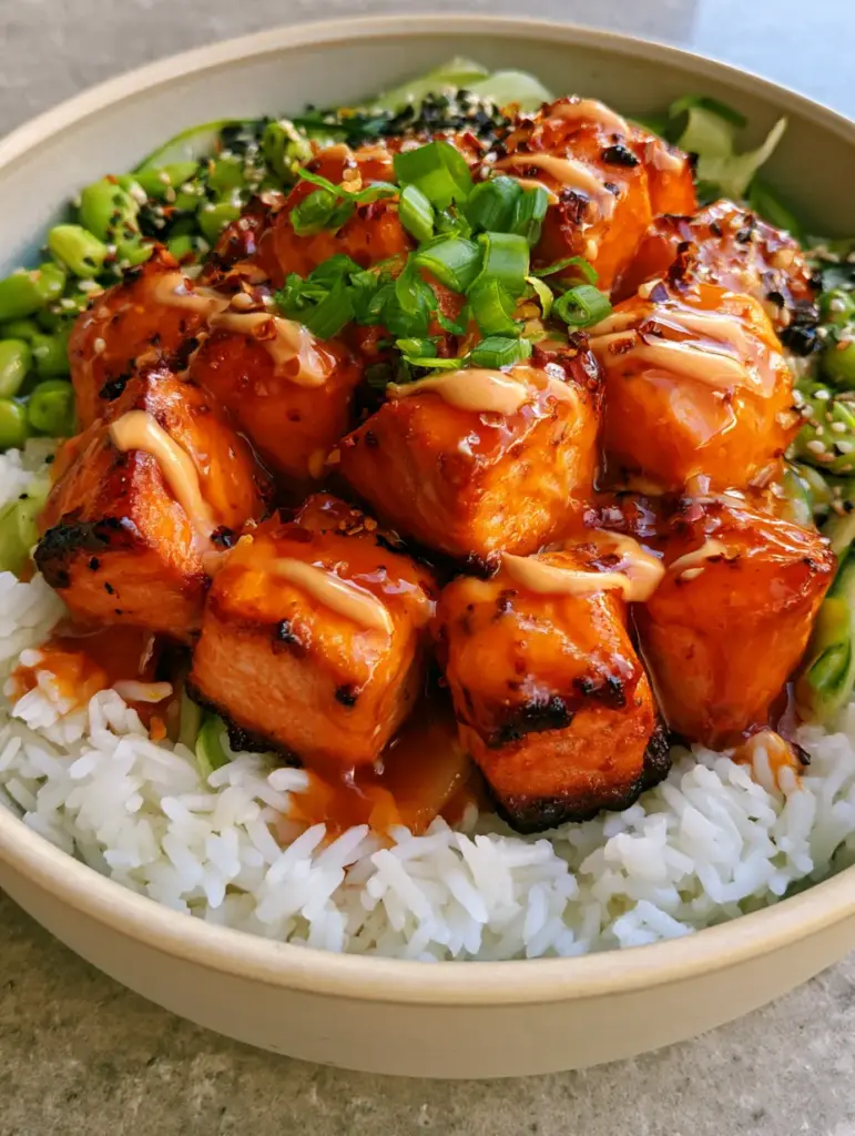 Close-up of glowing orange-red Sriracha Honey Salmon cubes with charred edges and sesame seeds.