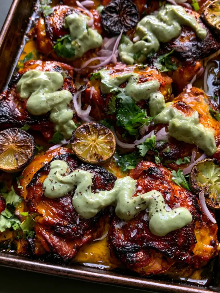 Spicy Peruvian Amarillo Chicken being drizzled with pale-green aji verde sauce alongside charred lime halves.