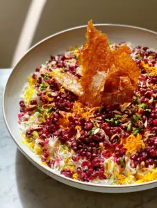 Top-down view of Persian Jeweled Rice showing the mosaic of saffron rice, barberries, and almonds in a white ceramic bowl.