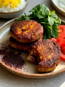 A close-up of three oval Persian Kotlet meat patties showing seared turmeric and onion flecks and a steaming moist interior.