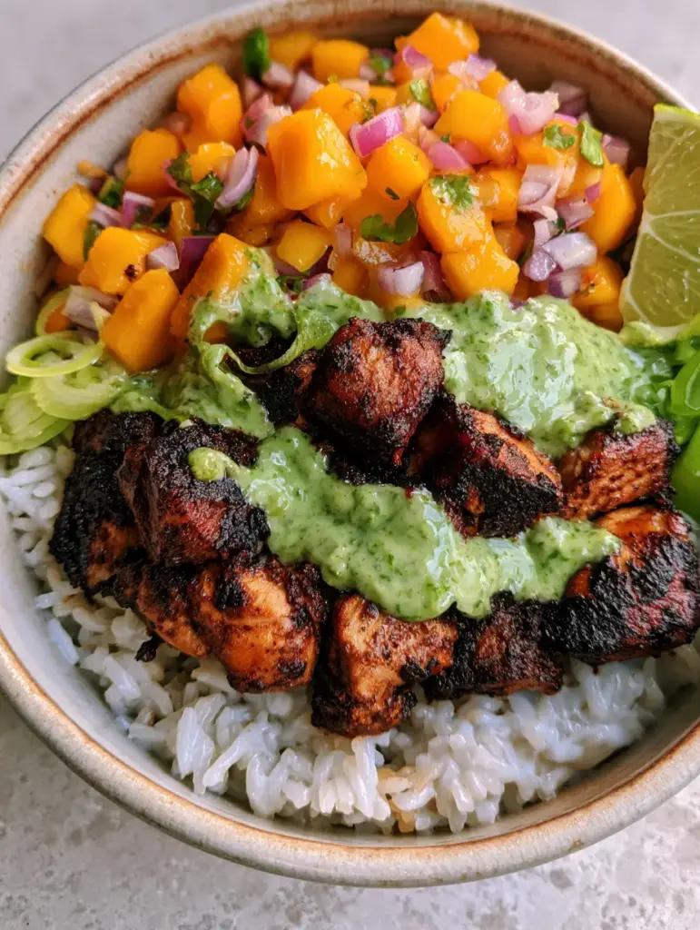 Jerk Chicken Bowl with Glistening Coconut Jasmine Rice and Mango Salsa 2 Macro view of charred jerk chicken breast cubes with a dark mahogany spice crust. (Jerk chicken bowl)