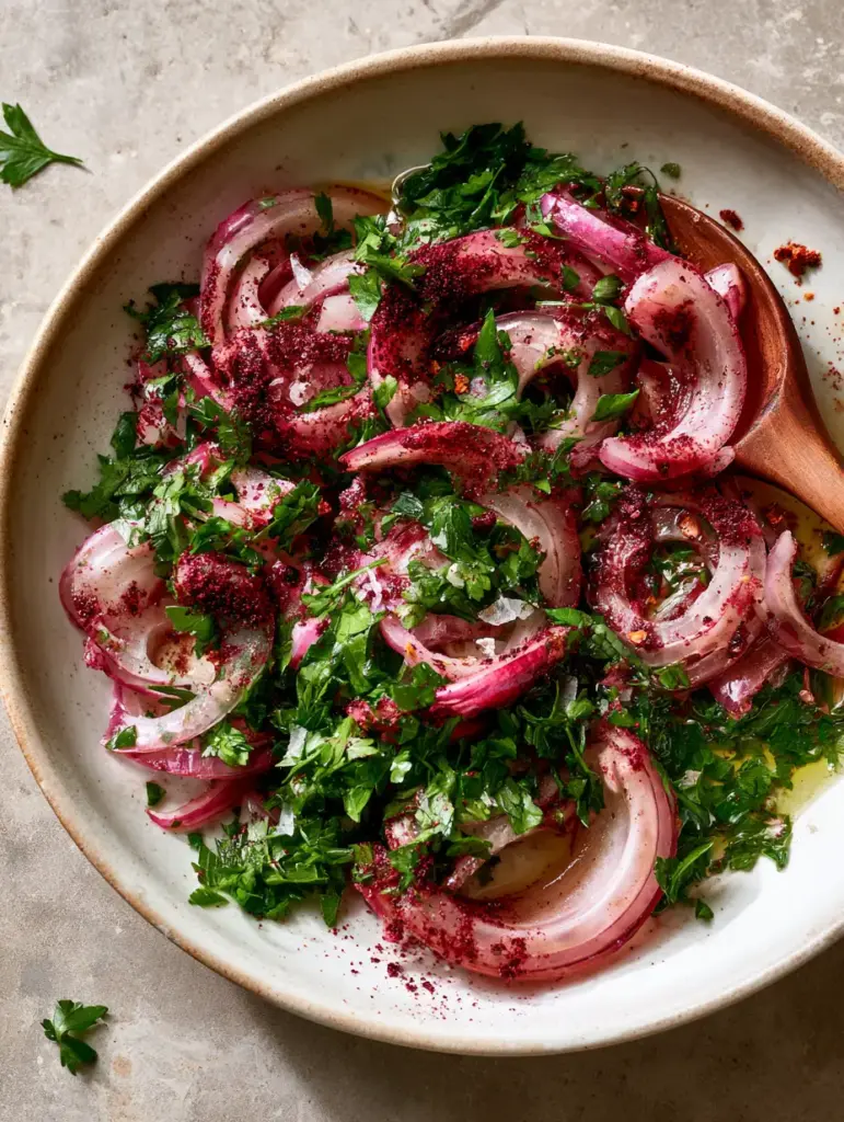 Glossy extra virgin olive oil shimmering over a sumac onion salad with lemon juice droplets and aleppo pepper.