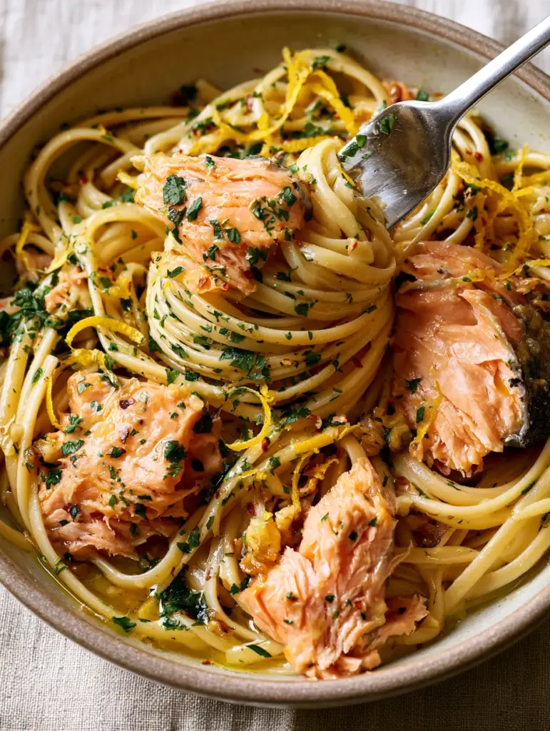 Canned Salmon Pasta with Garlic Butter and Lemon 1 A 45-degree angle close-up showing the glossy golden garlic butter sauce clinging to linguine strands and chunky pink salmon.