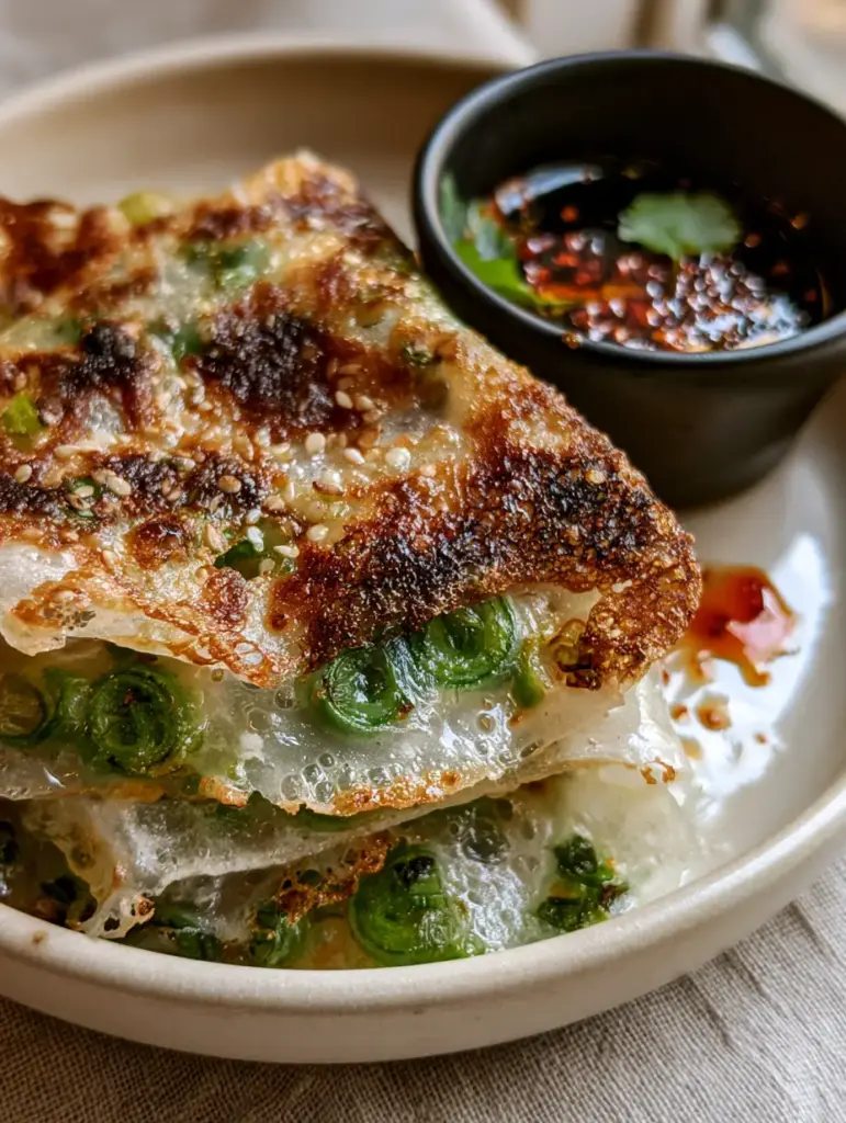 Macro shot of Rice Paper Scallion Pancakes with embedded scallions and glistening chili oil droplets in a black ramekin.