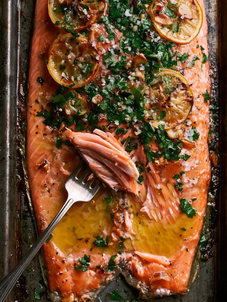 High-angle shot of a baked trout fillet with toasted garlic, parsley, and blistered skin edges.